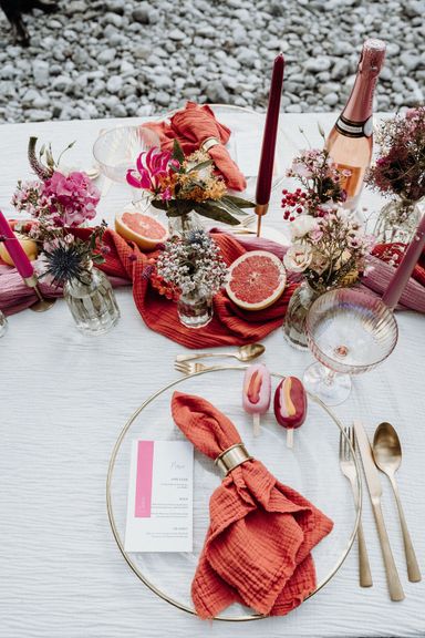 Bunte Hochzeits-Tischdekoration in orange und rosa mit Früchten, Sekt und kleinen Kuchen auf dem Tisch
