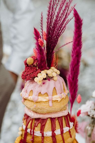 Detailaufnahme von einer Hochzeitstorte in Guggelhupf-Form in rosa, pink und hellgelb mit knalligen Trockenblumen