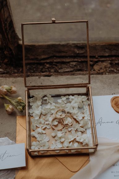 goldene Glasringdose mit Ringen und weißen Blütenblätter 